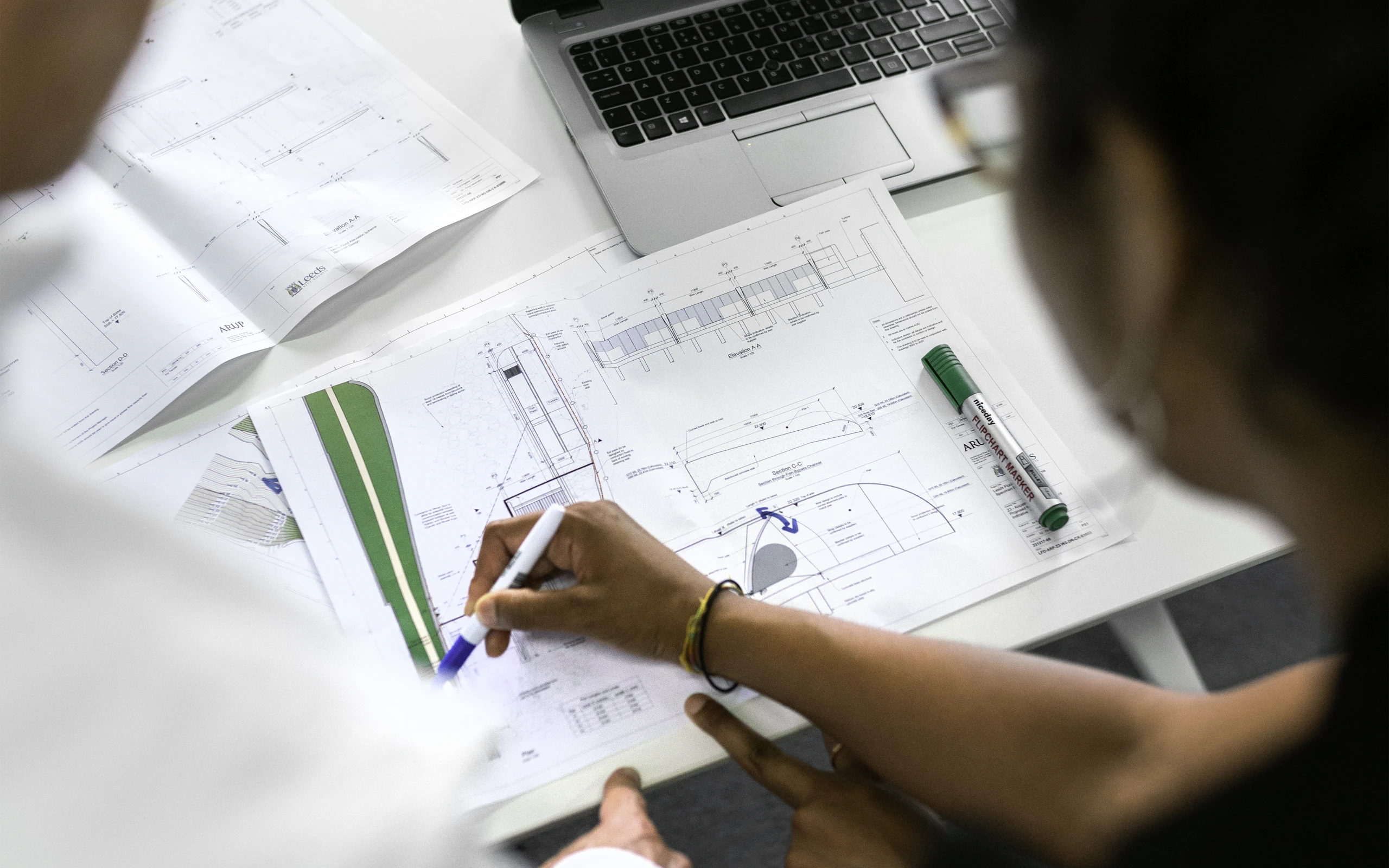 Two people reviewing architectural plans beside a laptop