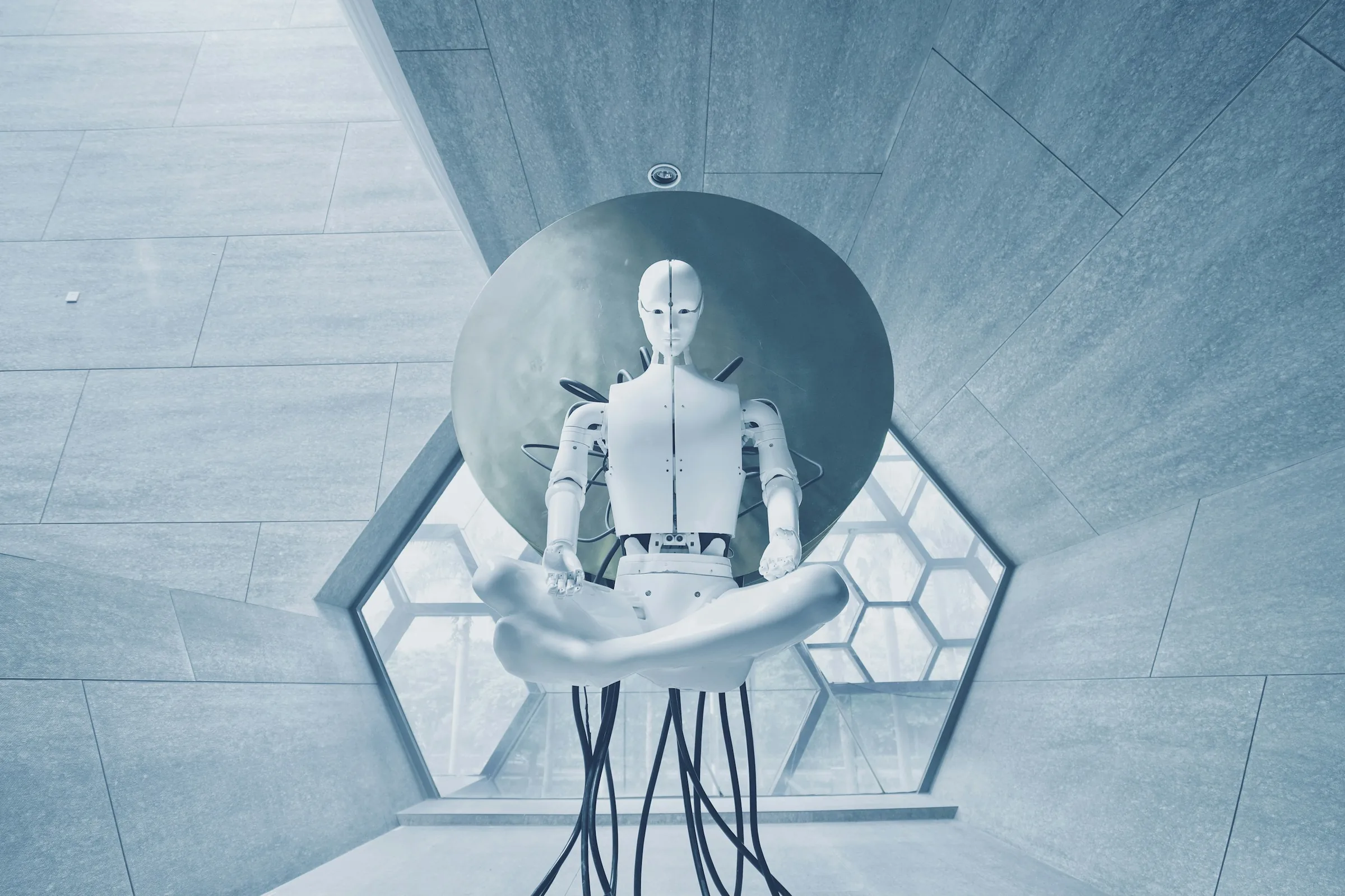 A white humanoid robot seated in a lotus position before a large circular disc